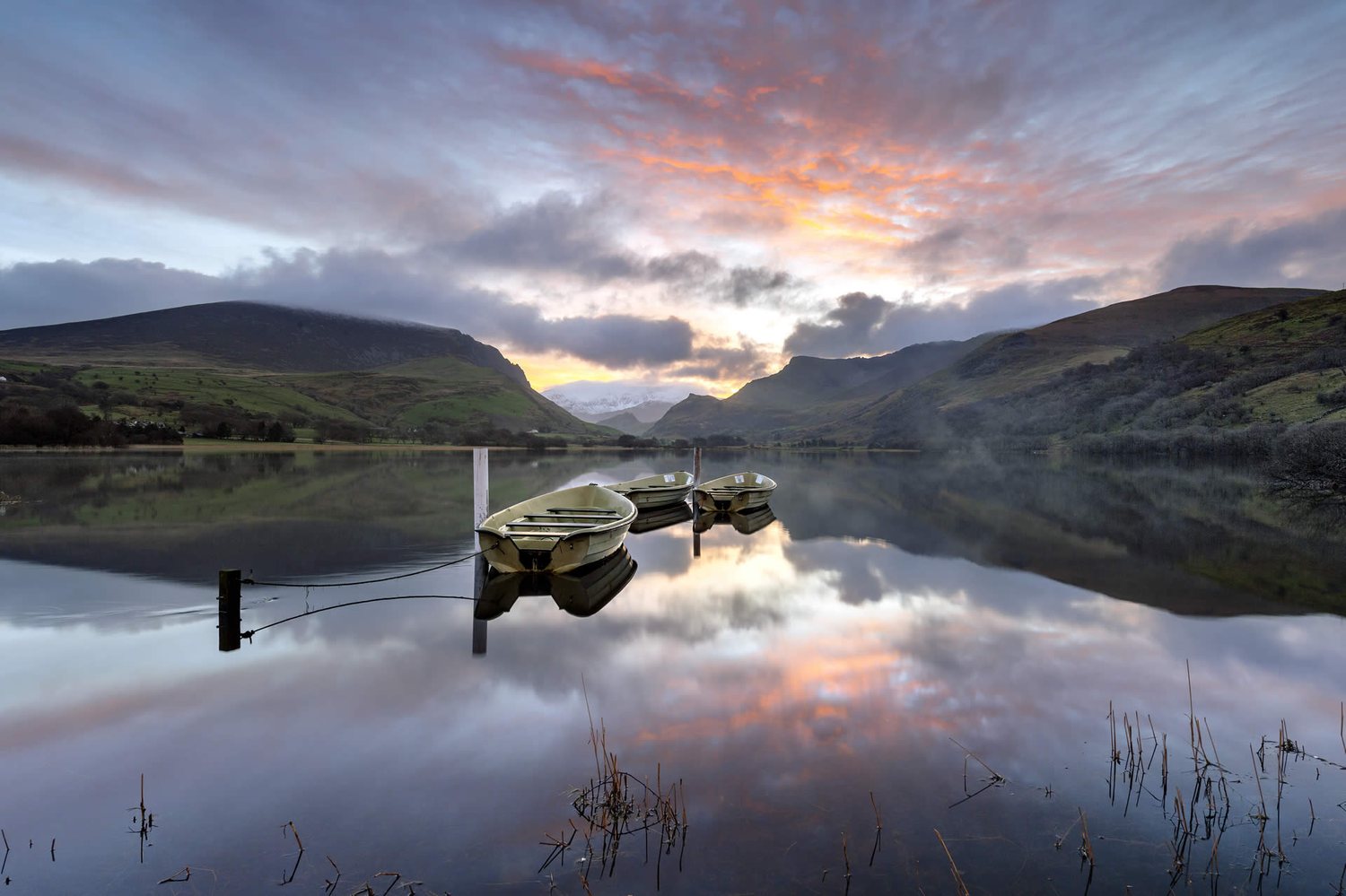 A calm, still lake at dawn surrounded by hills